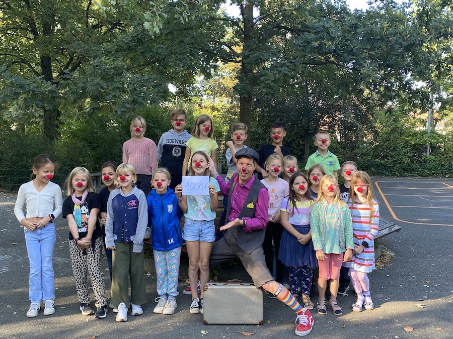 Die Kinder tragen bei der Übergabe der Spende an einen Klinikclown rote Clownsnasen.