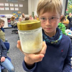 Ein Kind hält ein Schraubglas mit einem Butterklumpen hoch.