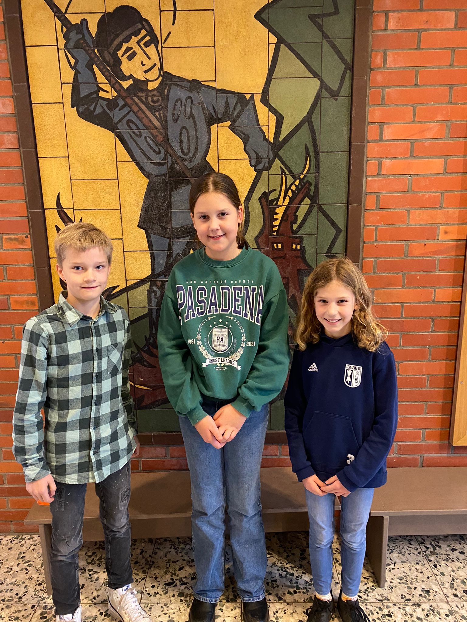 Die Klassensieger des Vorlesewettbewerbs Jonathan Nollmann (4c), Paula Klöpper (4a) und Tilda Weinberg (4b) stehen vor dem Mosaik des Hl. Georg.