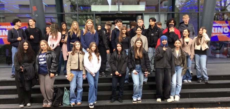 Eine große Gruppe von Schüler*innen der Gesamtschule Gronau und des Stedelijk Lyceum Enschede Zuid steht gemeinsam auf den Treppen vor dem Cinetech-Kino in Gronau. Die Jugendlichen posieren für ein Gruppenfoto nach einem gemeinsamen Austausch zum Thema Nachhaltigkeit. Im Hintergrund ist die Glasfassade des Kinos mit dem leuchtenden Schriftzug „Cinetech“ zu sehen.