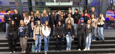 Austausch Gesamtschule Gronau und Stedelijk Lyceum Enschede Zuid Eine große Gruppe von Schüler*innen der Gesamtschule Gronau und des Stedelijk Lyceum Enschede Zuid steht gemeinsam auf den Treppen vor dem Cinetech-Kino in Gronau. Die Jugendlichen posieren für ein Gruppenfoto nach einem gemeinsamen Austausch zum Thema Nachhaltigkeit. Im Hintergrund ist die Glasfassade des Kinos mit dem leuchtenden Schriftzug „Cinetech“ zu sehen.