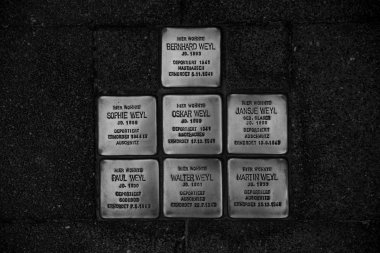 Schwarz-Weiß-Foto: Sieben Stolpersteine für Mitglieder der jüdischen Familie Weyl sind im Gehweg eingelassen; die Messingplatten tragen Name, Geburtsjahr, Deportationsort und Todesdatum der ermordeten Jüd*innen.