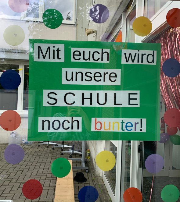 Grünes Plakat mit Aufschrift "Mit euch wird unsere Schule noch bunter!"