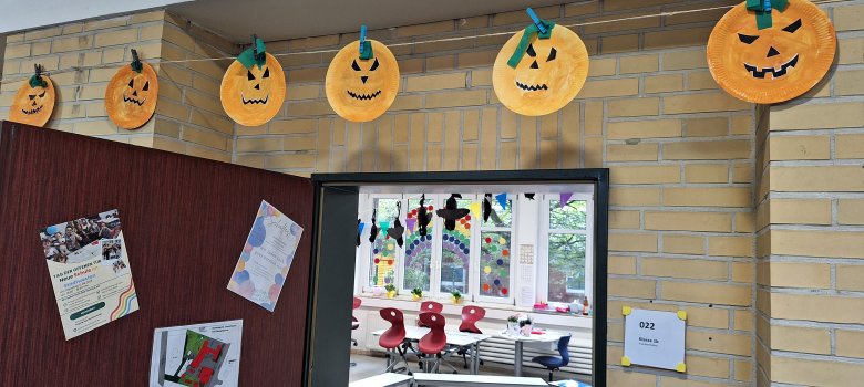 Gebastelte Halloweengesichter an einer Leine im Schulflur; der Betrachter kann in den Klassenraum schauen