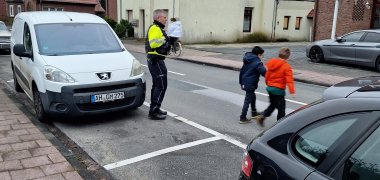 Zwei Kinder überqueren mit Polizist die Straße 