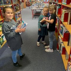 Drei Kinder suchen Bücher in der Bücherei