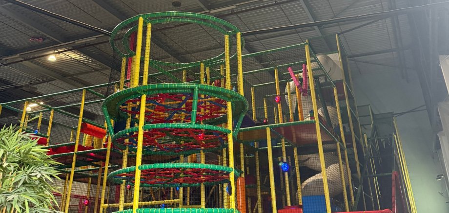 Das Foto zeigt einen bunten Kletterturm in einem Indoor Spielplatz mit verschiedenen Ebenen und Klettermöglichkeiten.