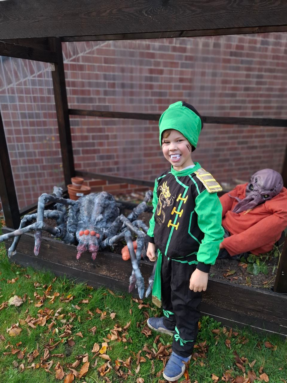 Das Foto zeigt ein einen Jungen im grünen Ninja Kostüm vor einer künstlichen Spinne und Horrorfigur.