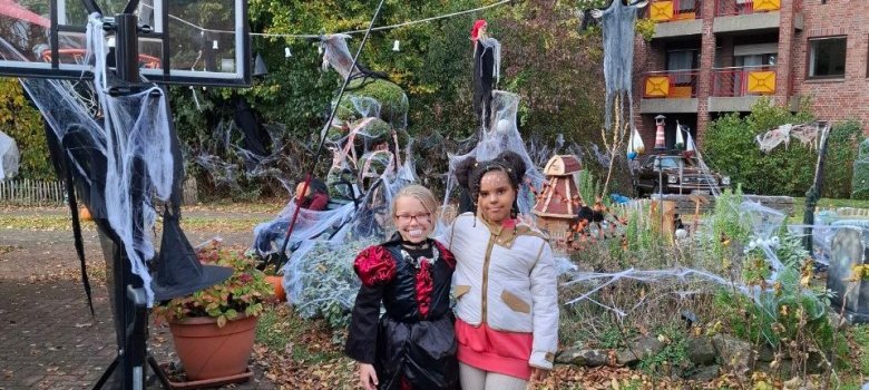 Das Foto zeigt zwei Mädchen, eine im Draculakostüm und eine sehr hell gekleidet vor einer kleinen Landschaft mit Spinnenweben.
