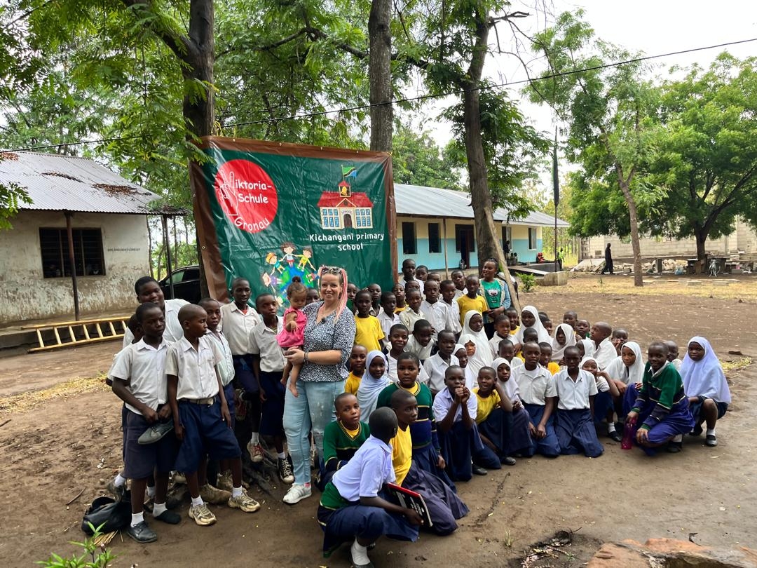 Janine Hundt und Kinder der Partnerschule in Tansania vor dem Schulbanner
