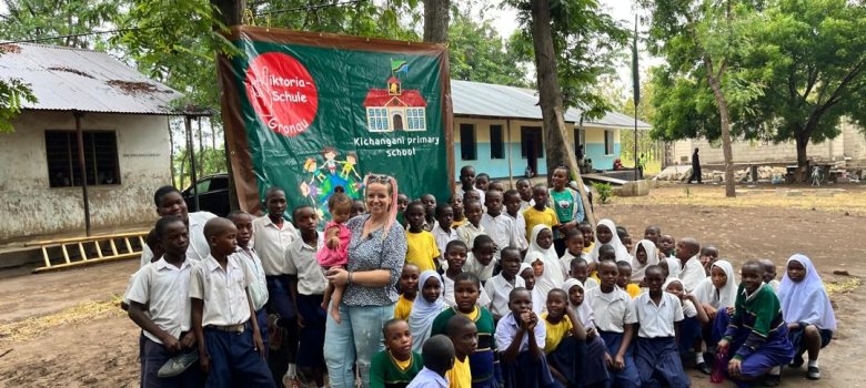 Janine Hundt und Kinder der Partnerschule in Tansania vor dem Schulbanner