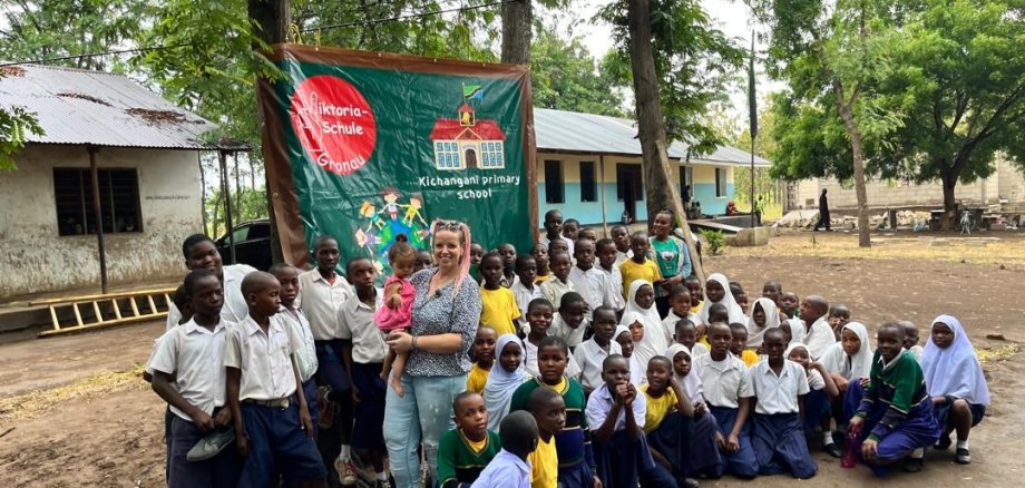 Janine Hundt und Kinder der Partnerschule in Tansania vor dem Schulbanner